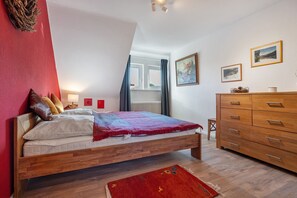 Un dormitorio con una cama de madera, un aparador, una ventana con cortinas y cuadros en la pared.