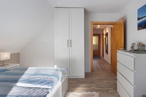 A bedroom with a bed, wardrobe, dresser, and a hallway leading to another room.