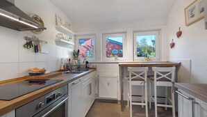 Una cucina moderna con mobili bianchi, un piano di lavoro in legno, un forno integrato e due sgabelli da bar.