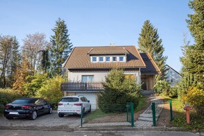 A two-story house with a tiled roof, a balcony, and a fenced driveway.