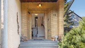 Una scala in mattoni conduce a una porta con il numero 12, un lampadario sopra e una piccola pianta in vaso sulla destra.