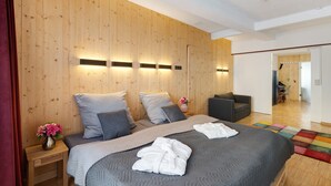 A modern bedroom with a wooden wall, a bed with grey bedding, a small bedside table with a vase of flowers, and a colorful rug on the floor.