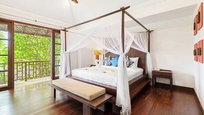 A bedroom with a four-poster canopy bed, a bench at the foot of the bed, a bedside table, and a view of lush greenery through large windows.