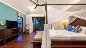 A bedroom with a four-poster bed, a television on a wooden cabinet, and a view of greenery through the window.