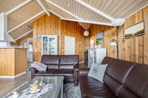 L’intérieur chaleureux d’un chalet avec des murs en bois, un canapé en cuir marron, une table basse en verre et un coin repas agrémenté d’un buffet blanc.