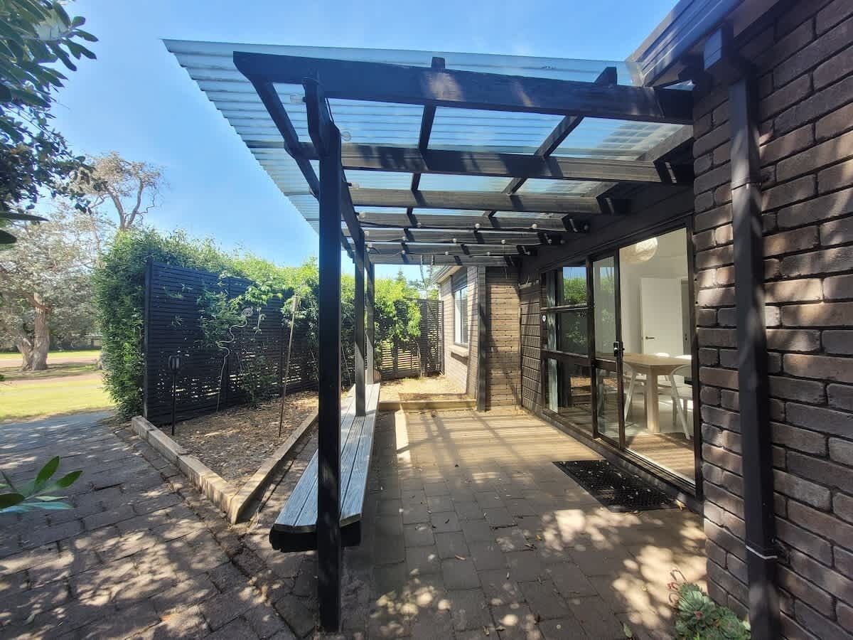 A covered patio area with a bench, a glass door leading to a room, and a brick wall.