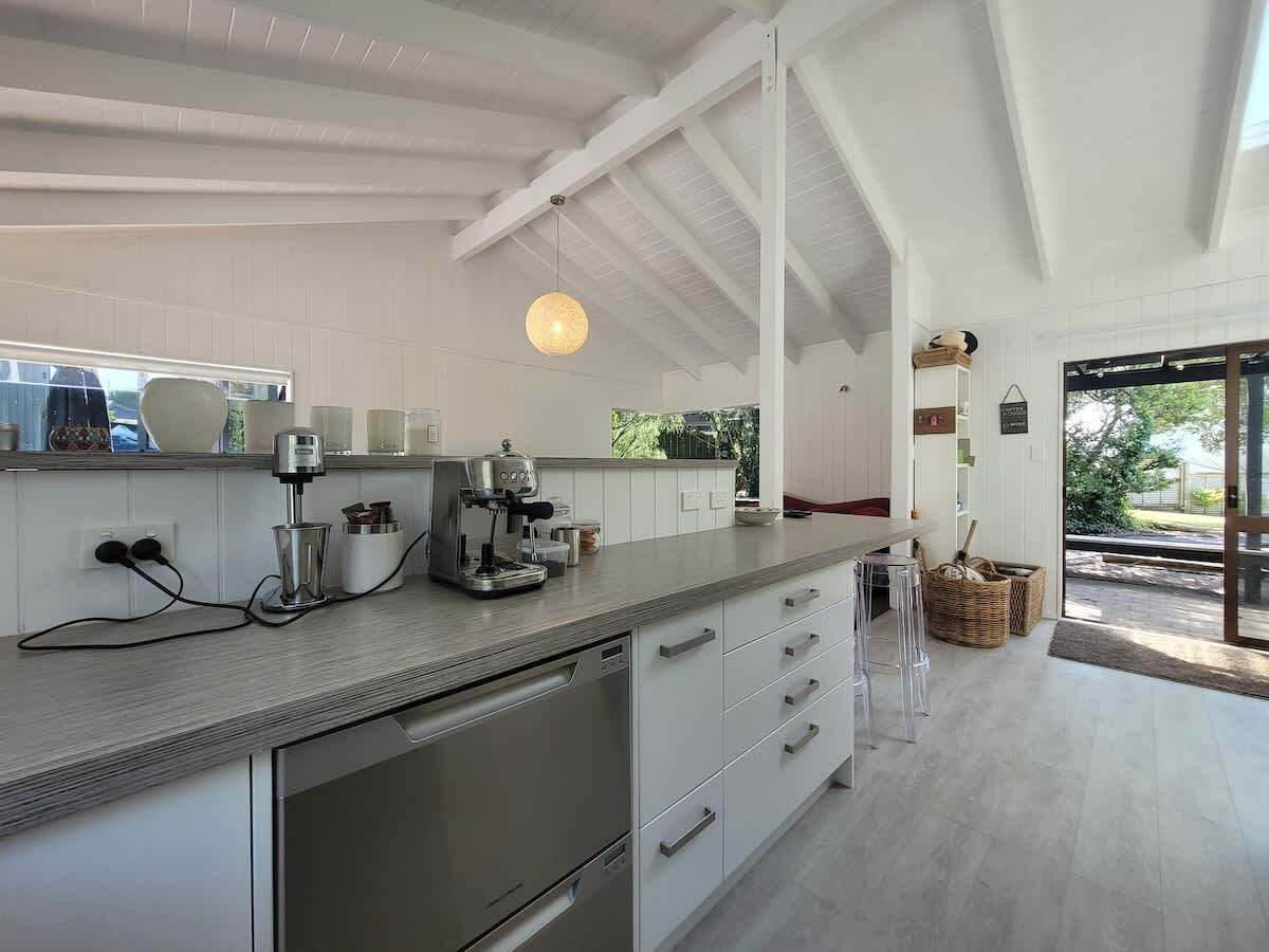 A modern kitchen with white cabinetry, a built-in oven, a coffee machine, and a hanging light fixture.