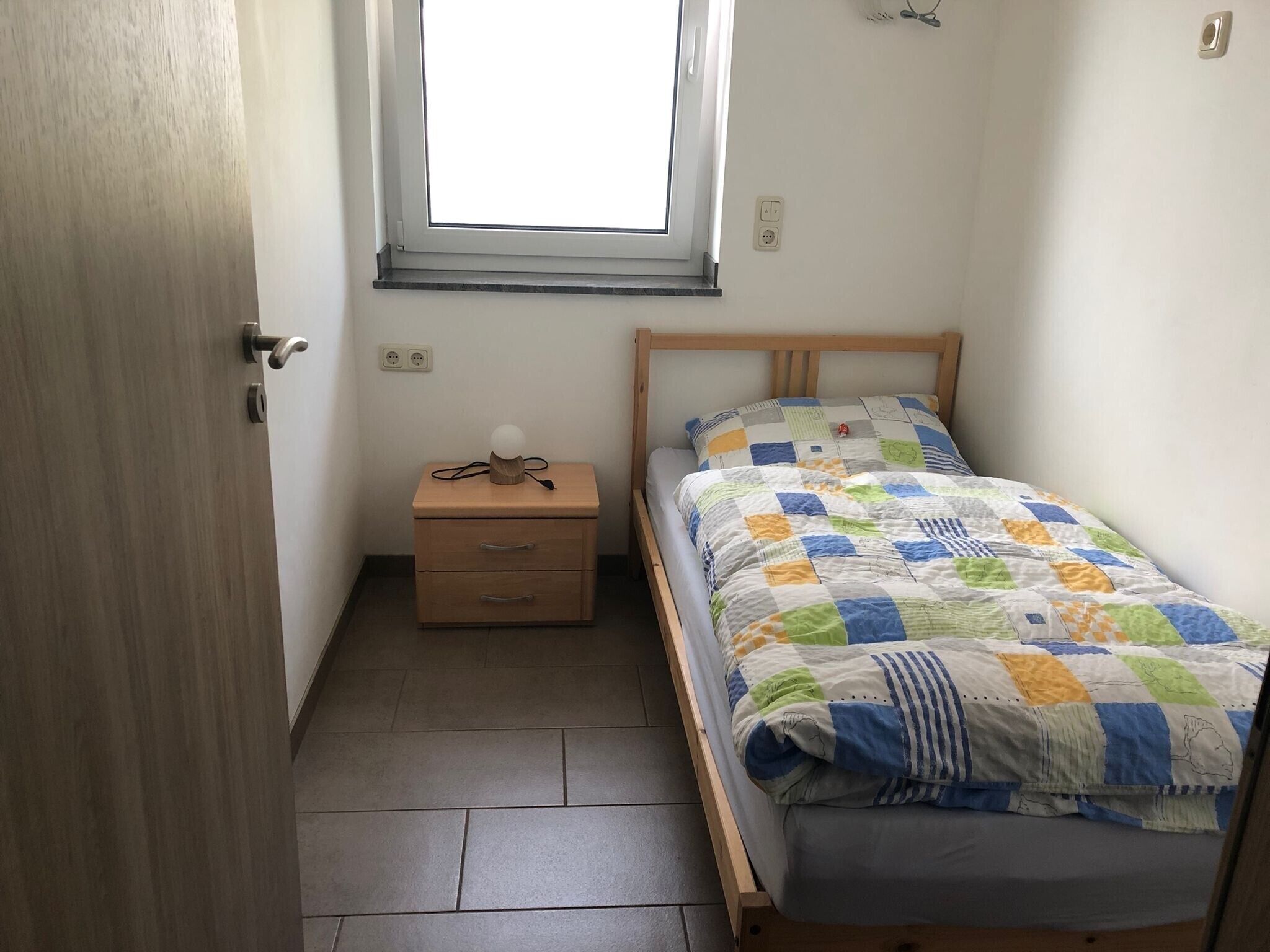 A bedroom with a bed, a nightstand, a window, and a door.