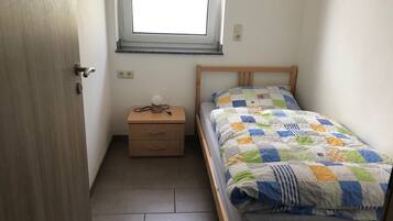 A bedroom with a bed, a nightstand, a window, and a door.