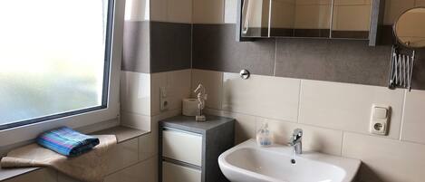 Ein Badezimmer mit Fenster, Waschbecken, Handtuch und Spiegel.