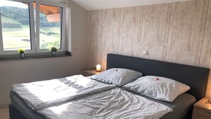 Un dormitorio con una cama, mesitas de noche, una ventana que ofrece vistas a zonas verdes y un panel de pared de madera.