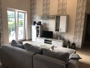 Un salon avec un canapé, une télévision et un balcon offrant une vue agréable.