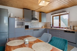 A kitchen with grey cabinets, a wooden ceiling, and a dining table with placemats. - Jogis Paradise: Quiet Apartment, Balcony, Outdoor Sauna & Wi-Fi (Stockach)