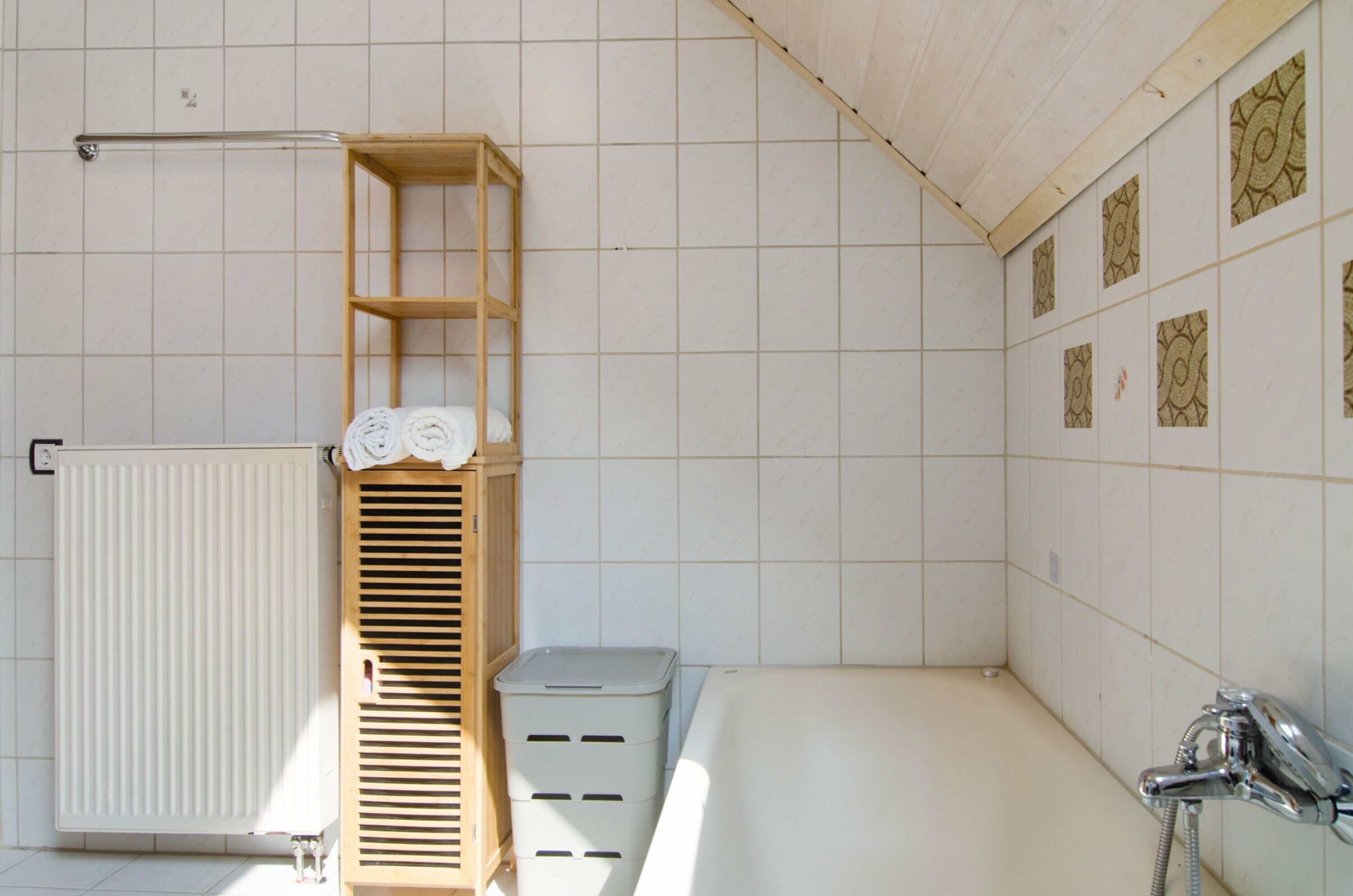Ein Badezimmer mit einer Badewanne, einem hölzernen Ablagebrett mit Handtüchern, einem Heizkörper und gemusterten Fliesen an der Wand.
