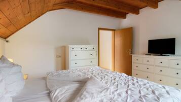 A bedroom with a wooden ceiling, a bed with white bedding, a dresser with drawers, and a television on top.