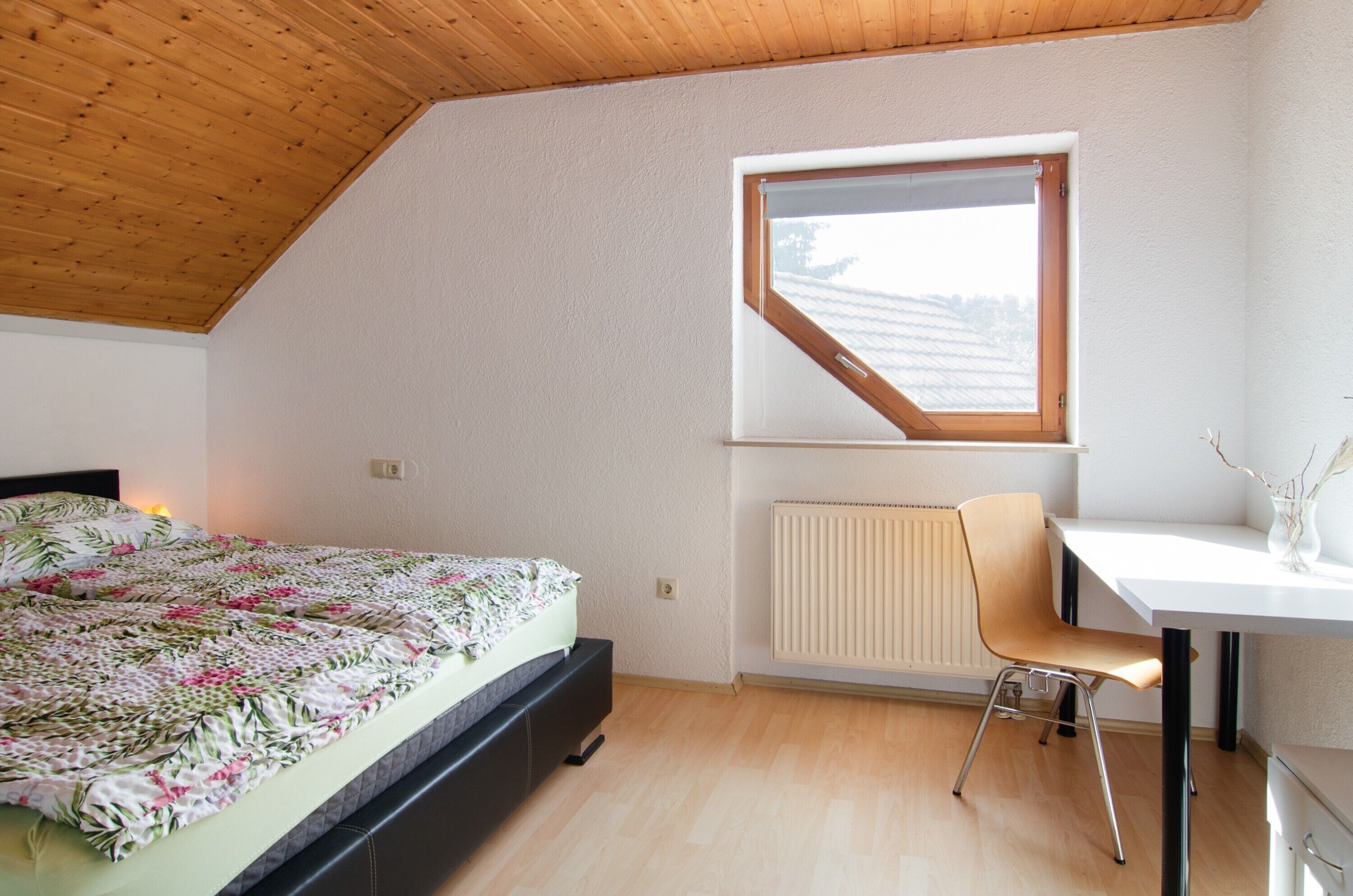 Une chambre à coucher avec un lit, un bureau, une chaise, un radiateur et une fenêtre.