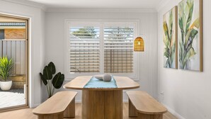 A dining area with a round table and two benches, a window with blinds, a potted plant, and a wall-mounted light fixture.