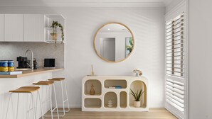 A modern kitchen with a white countertop, bar stools, a round mirror, and a built-in cabinet with shelves.