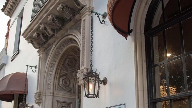 Un edificio con detalles arquitectónicos ornamentales, incluyendo un amplio arco de entrada y molduras decorativas. Un cartel anuncia un lugar que ofrece helados y pasteles.