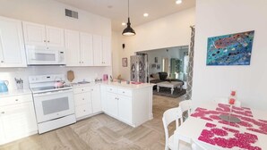 Una cocina moderna con armarios blancos, una isla central y un comedor con una mesa dispuesta para dos personas.