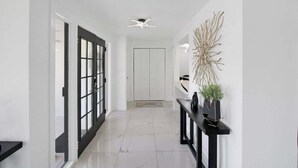Ein moderner Flur mit einer Tür in schwarzem Rahmen, einem Deckenventilator und einer an der Wand befestigten Pflanze.