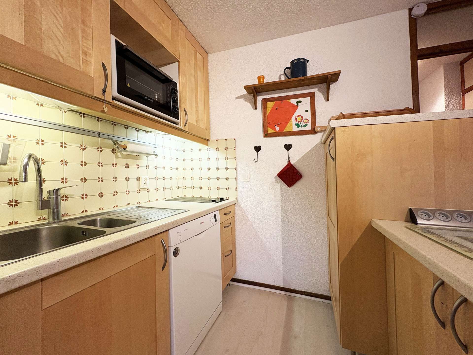 A compact kitchen with wooden cabinets, a stainless steel sink, a microwave, and a dishwasher.