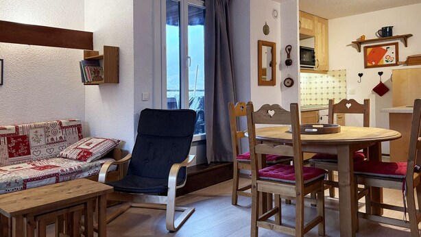 A cozy living room with a sofa, a dining table with chairs, and a window with curtains.