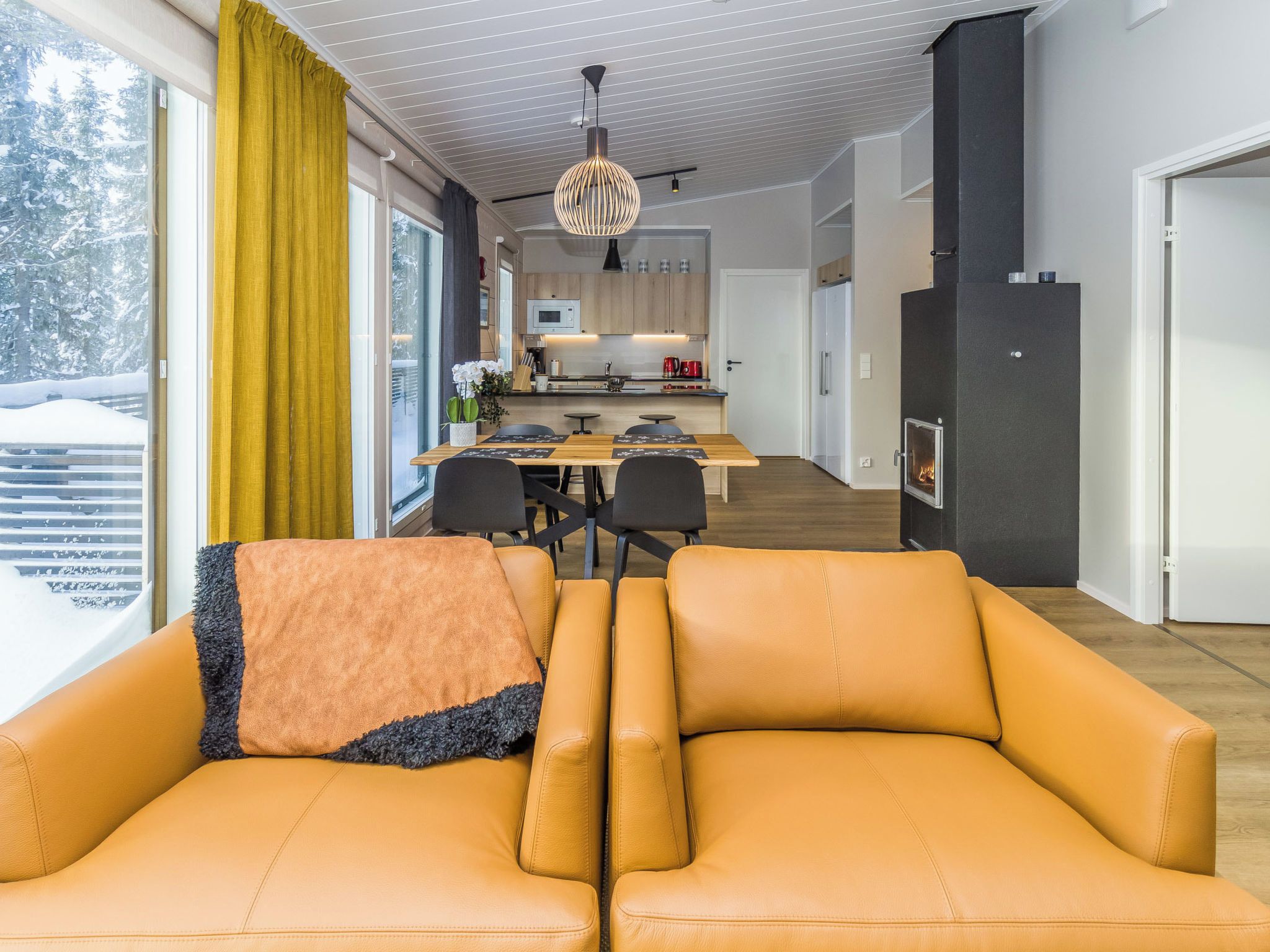A modern living room with a sofa, a dining area with a table and chairs, and a kitchen with wooden cabinets.