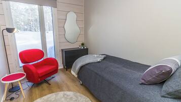 A bedroom with a bed, a red chair, a small table, a lamp, and a window with a view of trees.