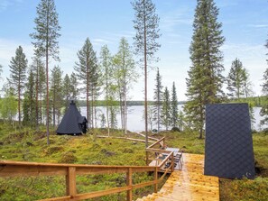 A wooden deck leading to a conical structure near a lake, surrounded by tall trees.