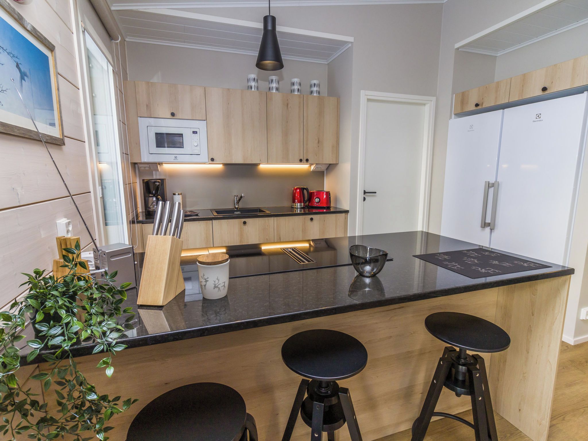Een moderne keuken met een centraal eiland, barkrukken, een magnetron, een koffiezetapparaat en een koelkast.
