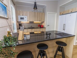 Una cocina moderna con una isla central, taburetes de bar, microondas, cafetera y refrigerador.