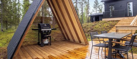 An outdoor wooden deck with a grill, a table with chairs, and a house in the background.