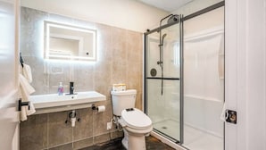 Une salle de bain moderne avec une douche à parois de verre, des toilettes blanches et un meuble-lavabo doté d’un miroir et d’un porte-serviettes.