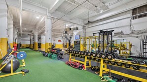 Une salle de sport équipée de matériel de musculation, dotée d’un sol vert et d’un panier de basket.