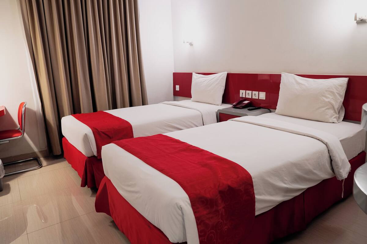 A hotel room with two beds, each with red and white bedding, a red headboard, and a bedside table with a phone.
