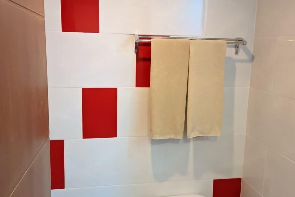 A bathroom with white and red tiles, a towel rack with a beige towel, and a shower area.