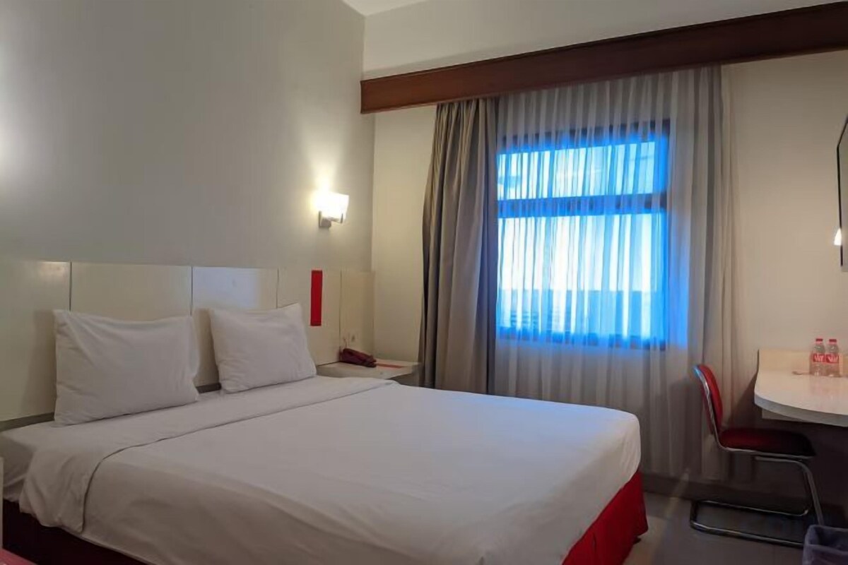 A hotel room with a bed, a desk, a chair, and a window with curtains.