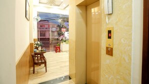 A hotel lobby with a reception desk, a small table with a vase of flowers, and an elevator with a digital display. - Co Hong Hotel DL - by BAY LUXURY (Lam Vien - Da Lat)
