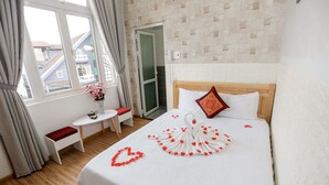 A hotel room with a bed, a small table with a chair, a window with curtains, and a view of buildings outside. - Co Hong Hotel DL - by BAY LUXURY (Lam Vien - Da Lat)