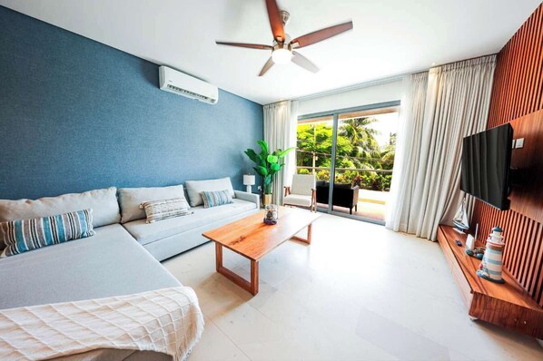 Relax in a serene space with a view of lush greenery, featuring a large window, flat-screen TV, and comfortable seating area.