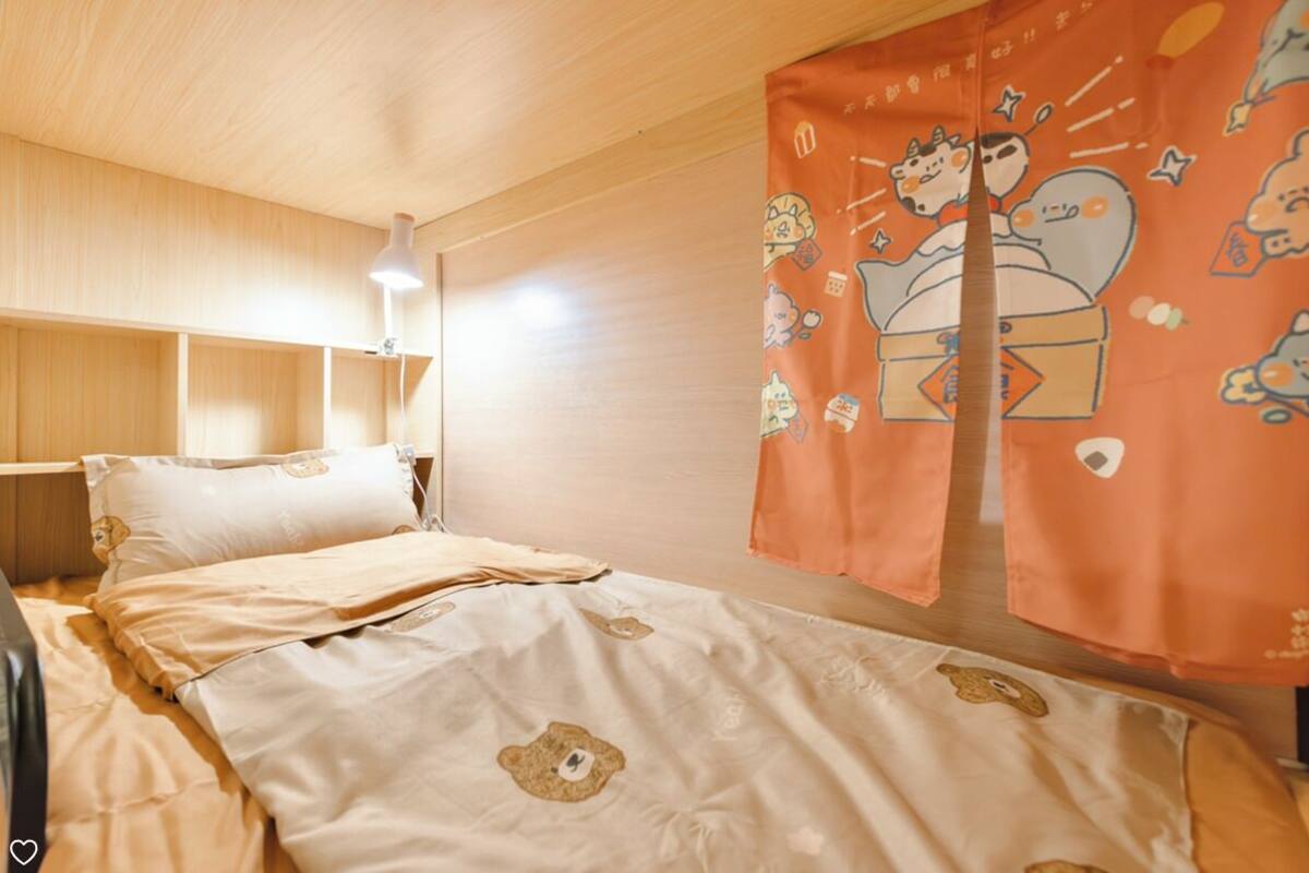 A room with a bed, a bedside table, a lamp, and a curtain with cartoon characters.