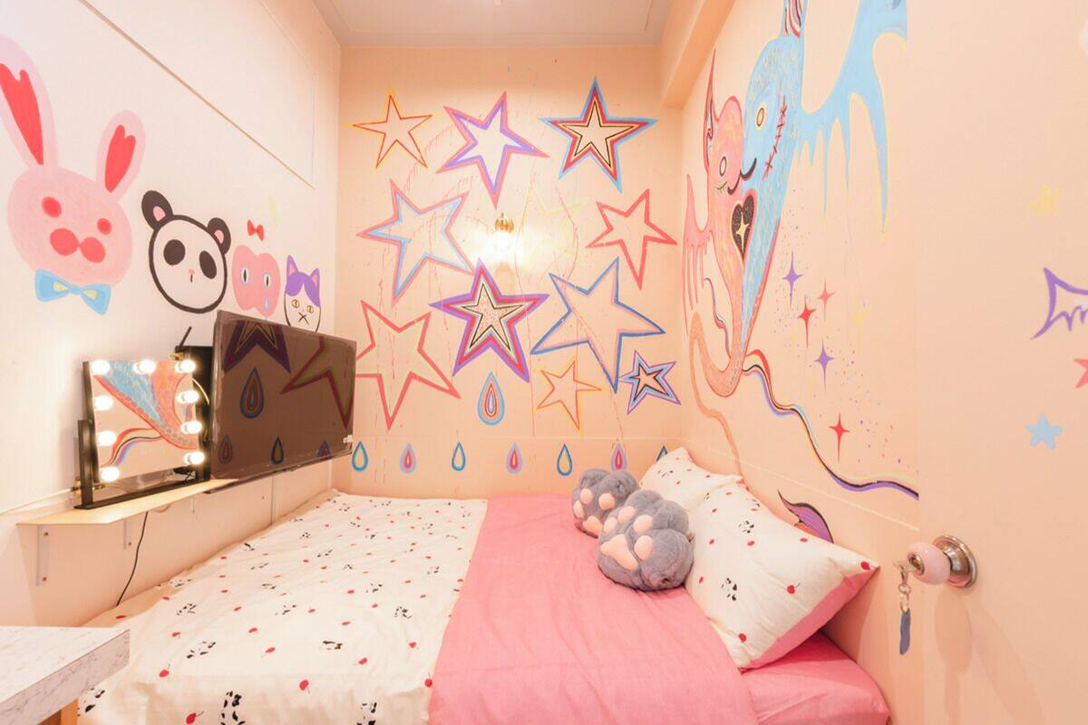 A bedroom with a bed, a vanity with lights, and wall decorations including stars and cartoon characters.