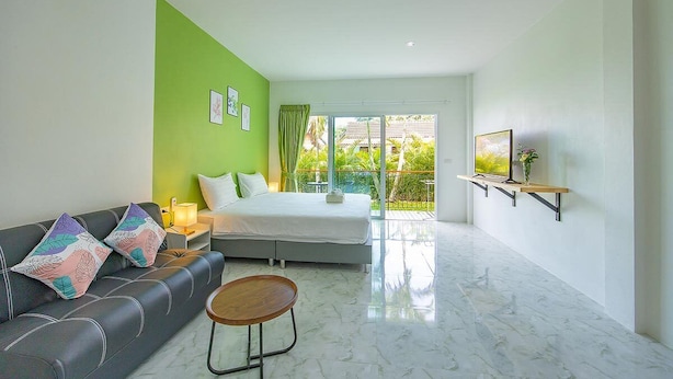 A modern hotel room with a green accent wall, a bed, a sofa, a small table, and a TV mounted on the wall. - Karon Hotel  at 22 (Karon)