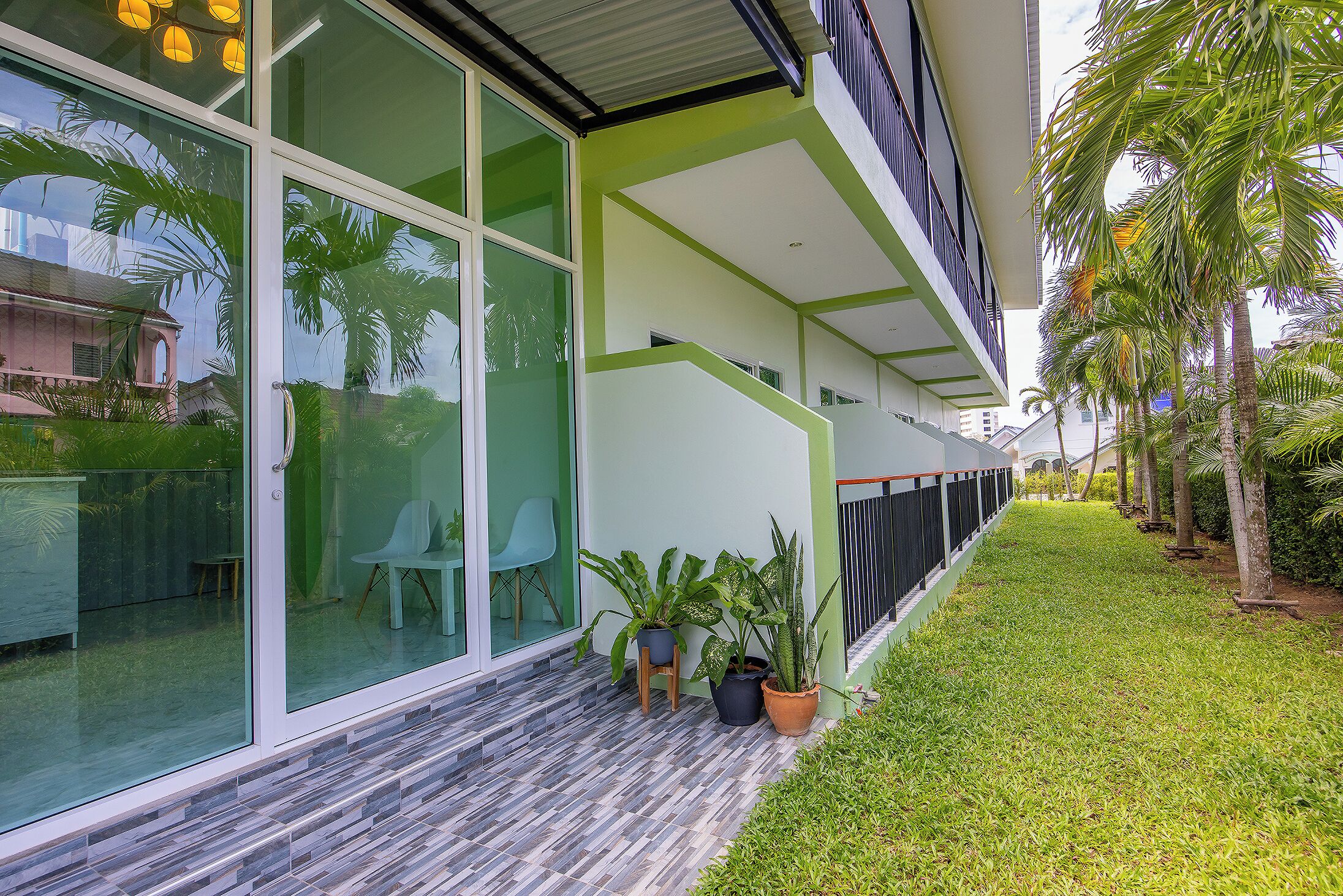 Un edificio moderno con amplios ventanales, fachada verde y un pequeño patio con plantas en macetas.