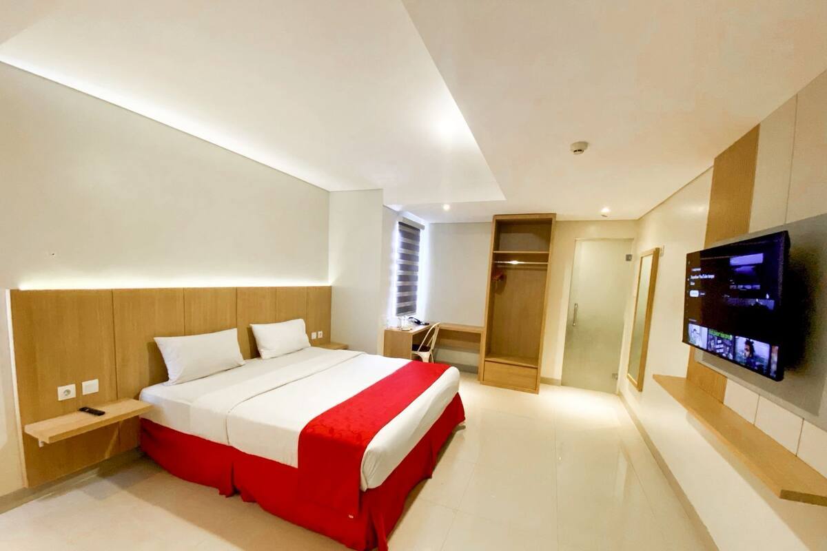 Ein modernes Hotelzimmer mit einem großen Bett, einem Fernseher, einem Schrank und einem Schreibtisch.