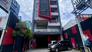 A building with a prominent red and grey facade, a visible entrance, and a parked car in front. - Brothers Inn Babarsari Yogyakarta (Depok)