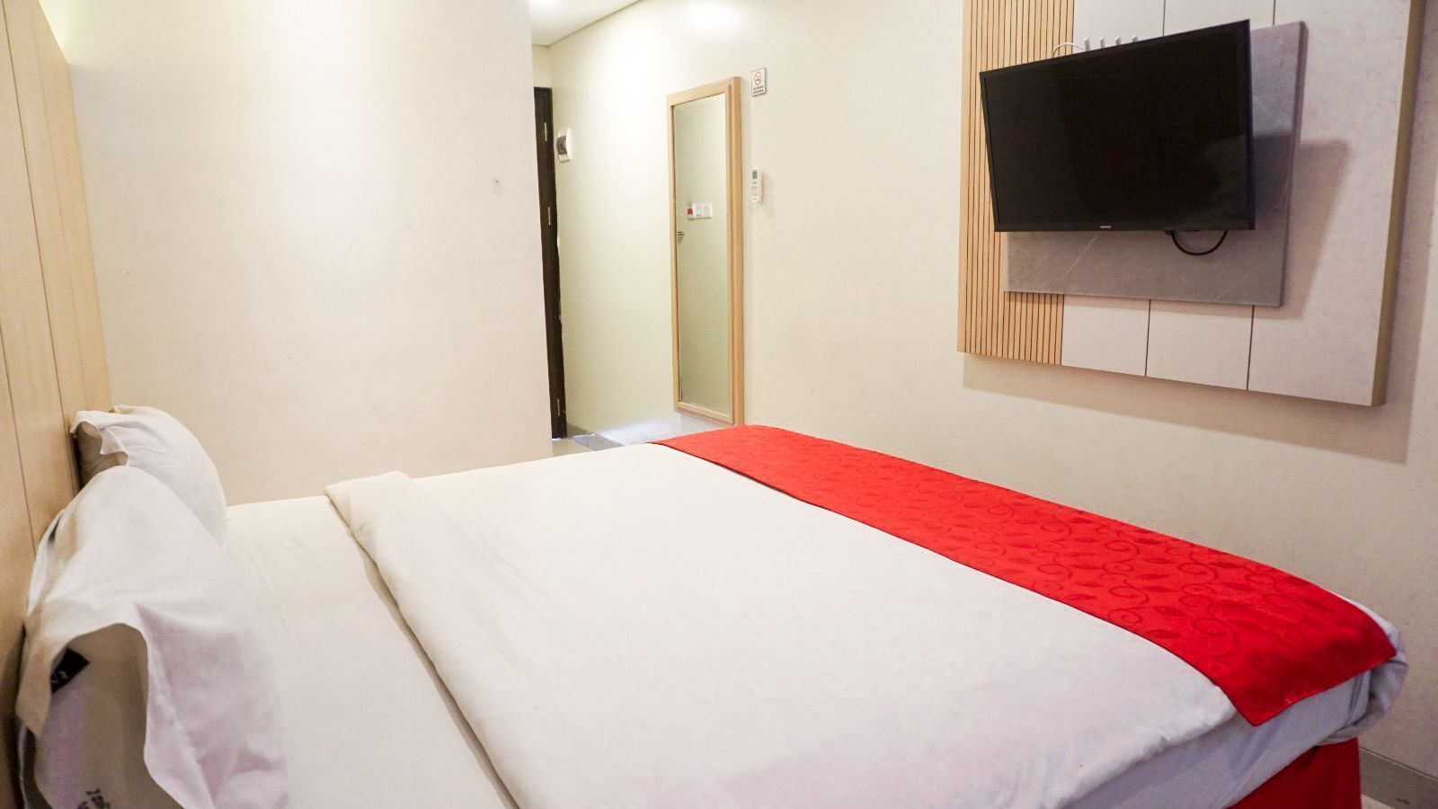 A hotel room with a bed, a television mounted on the wall, and a red runner across the bed.