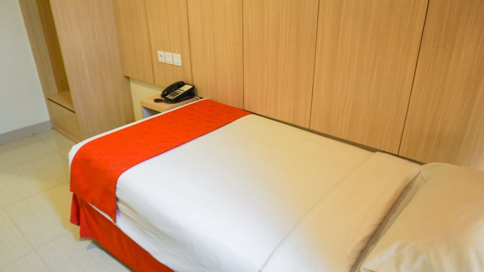 Een hotelkamer met een bed, een nachtkastje met een telefoon en houten lambrisering.