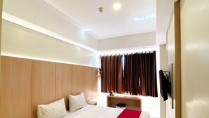 A modern hotel room with a large bed, wooden headboard, bedside tables, and a desk with a chair. - Brothers Inn Babarsari Yogyakarta (Depok)